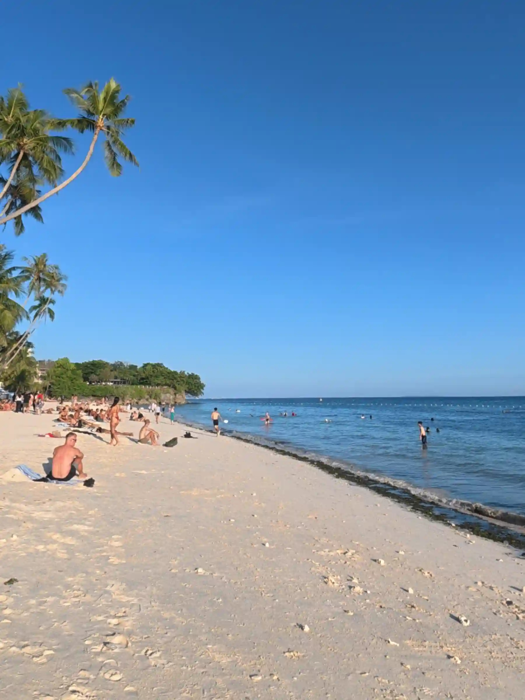 Tourists sunbathing and swimming along the white sand shore of Alona Beach near Henann Resort in Panglao Bohol under a clear blue sky