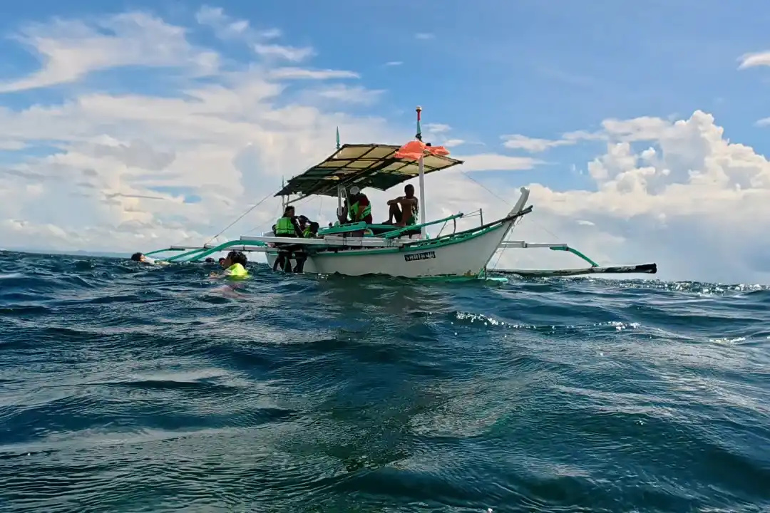 Bangka outrigger boat with passengers on choppy open water with snorkelers in the sea beside it at Villa Del Prado Sariaya Quezon