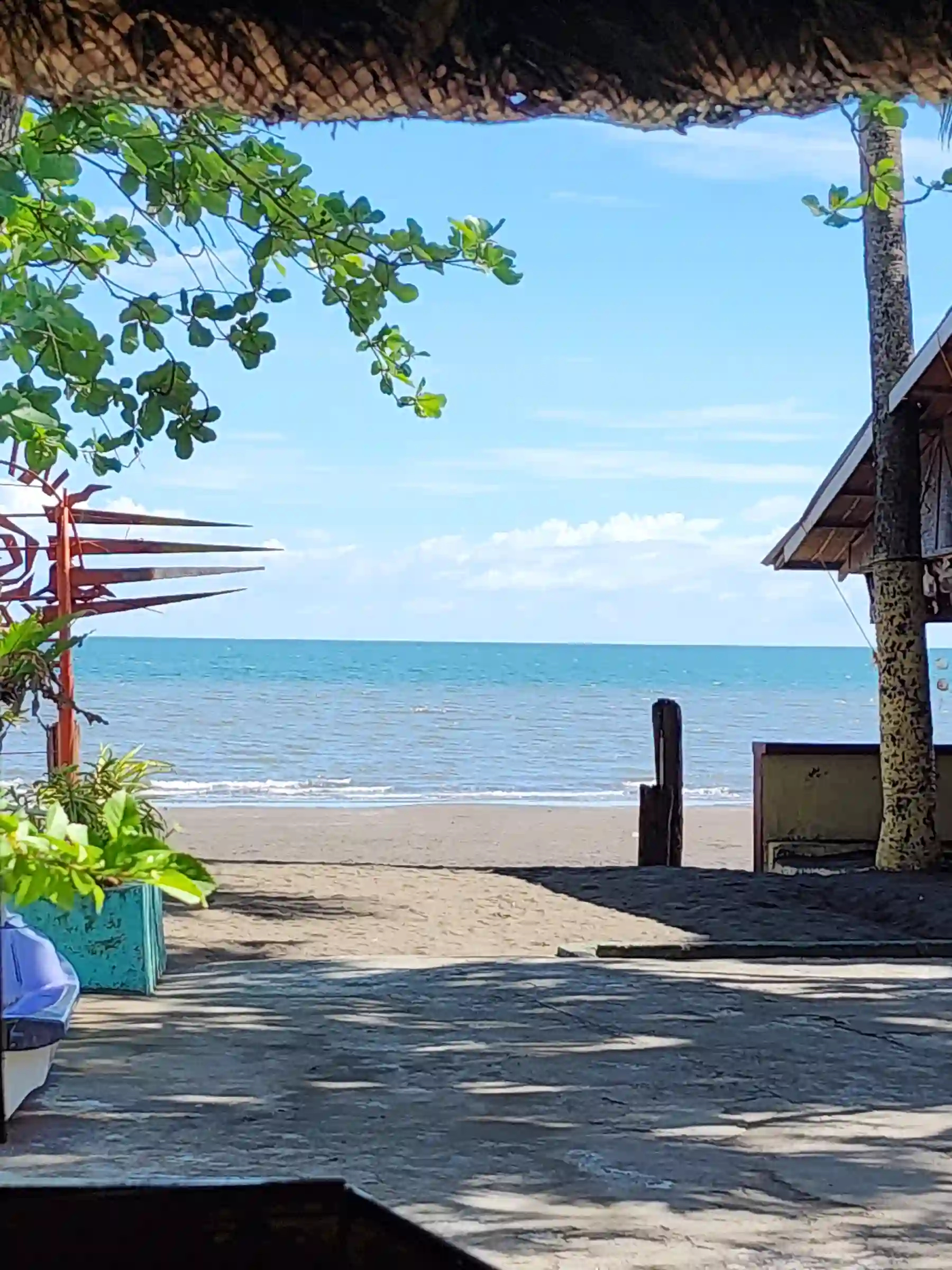 View of dark sand beach and calm sea framed by the open face of a nipa hut at Villa Del Prado Pool and Beach Resort in Sariaya Quezon