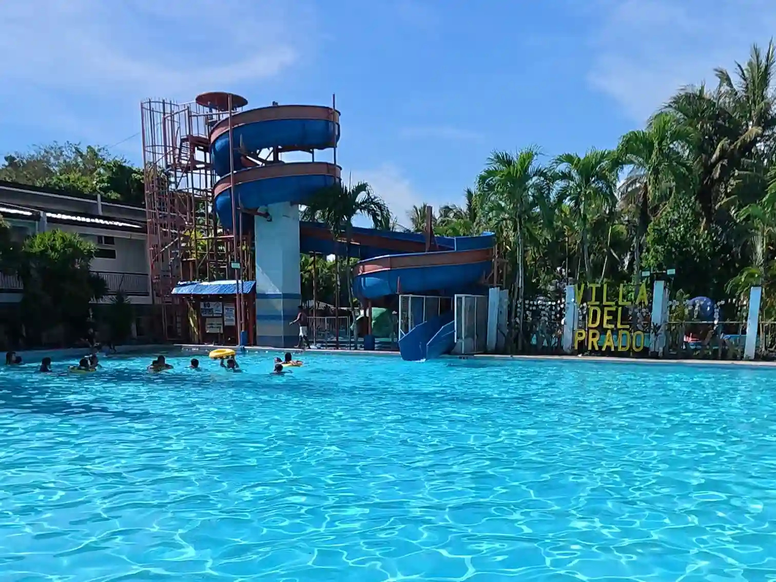 Large pool with blue spiral water slide and Villa Del Prado resort signage surrounded by palm trees in Sariaya Quezon