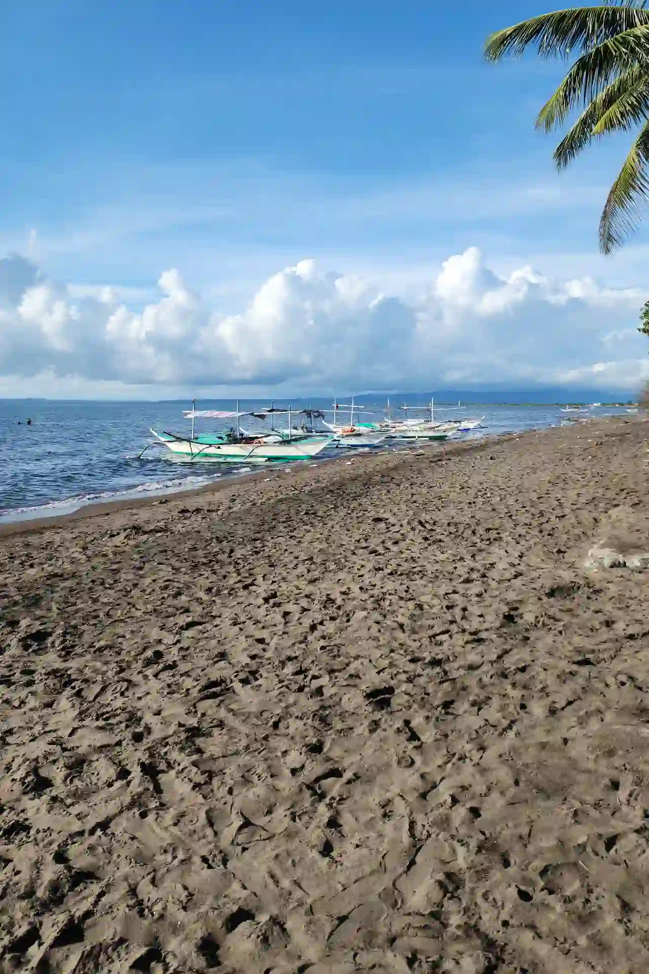 Dark volcanic sand shore with bangka boats moored at the waterline at Villa Del Prado Pool and Beach Resort in Sariaya Quezon