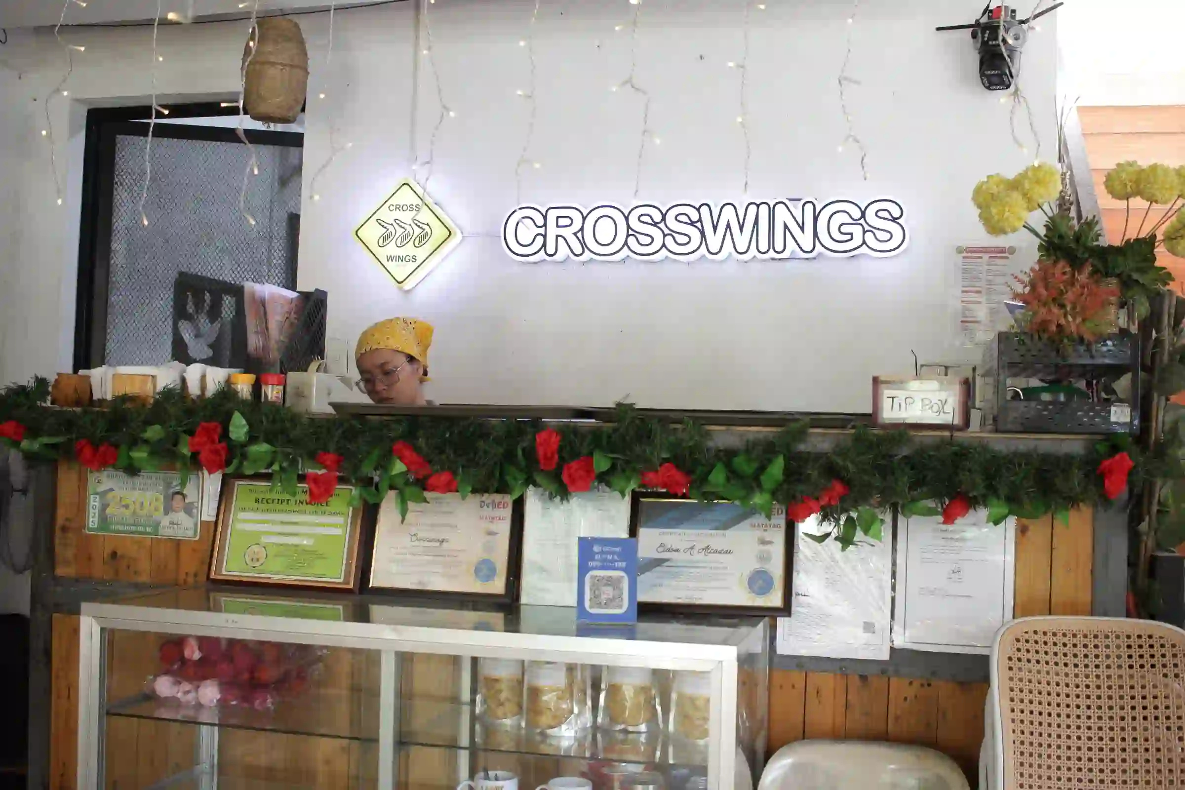 Crosswings illuminated neon sign above the service counter with a staff member and framed certificates in Alfonso Cavite