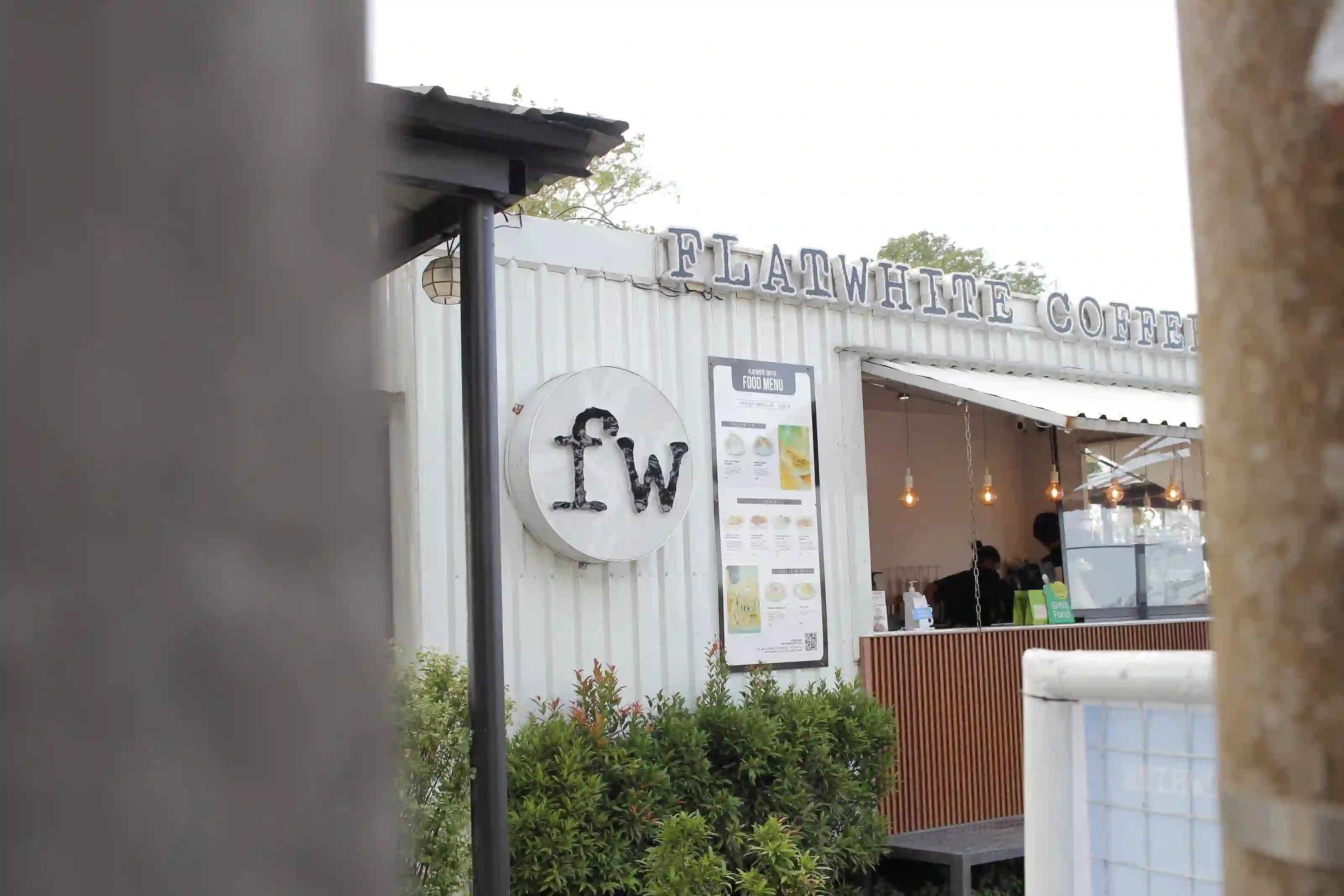 Flatwhite Coffee white container kiosk partially framed by a lamppost and concrete pillar along Tagaytay Nasugbu Highway in Cavite