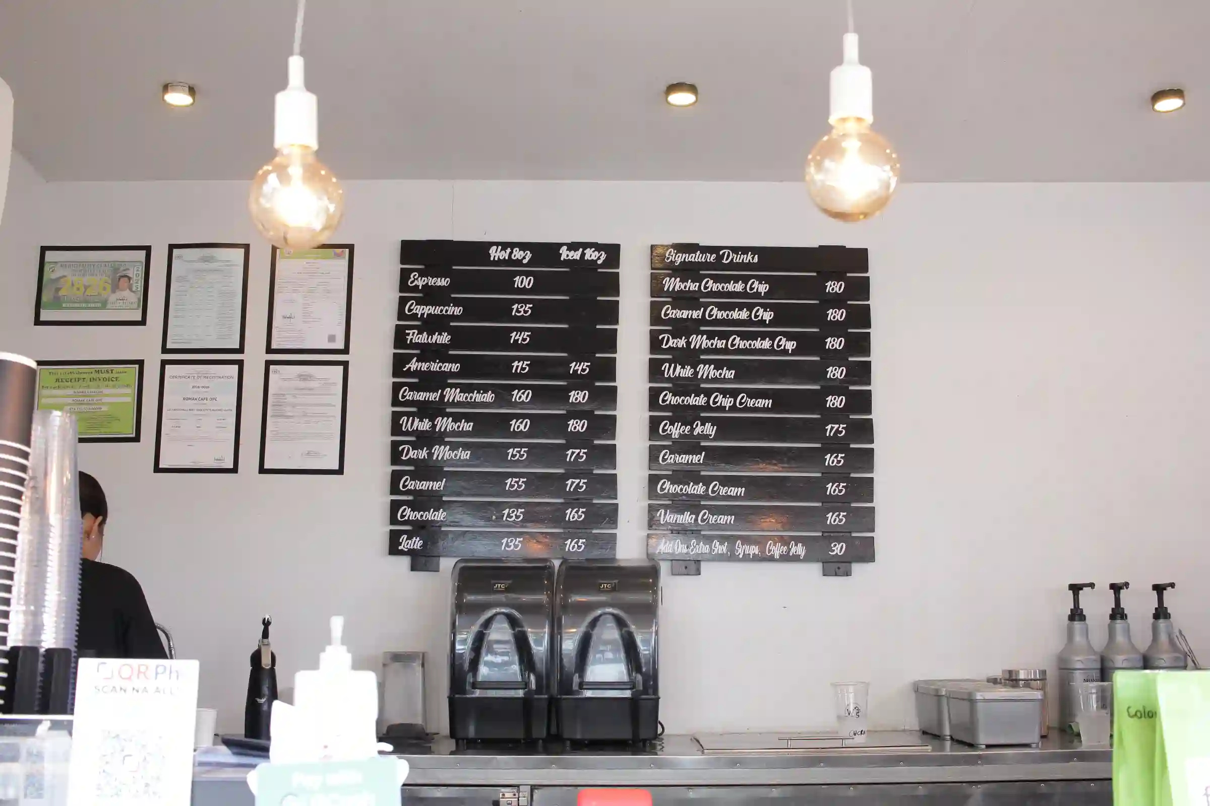 Blackboard menu and pendant lights above the counter at Flatwhite Coffee Ronak Cafe in Alfonso Cavite showing drink prices from 100 to 180 pesos
