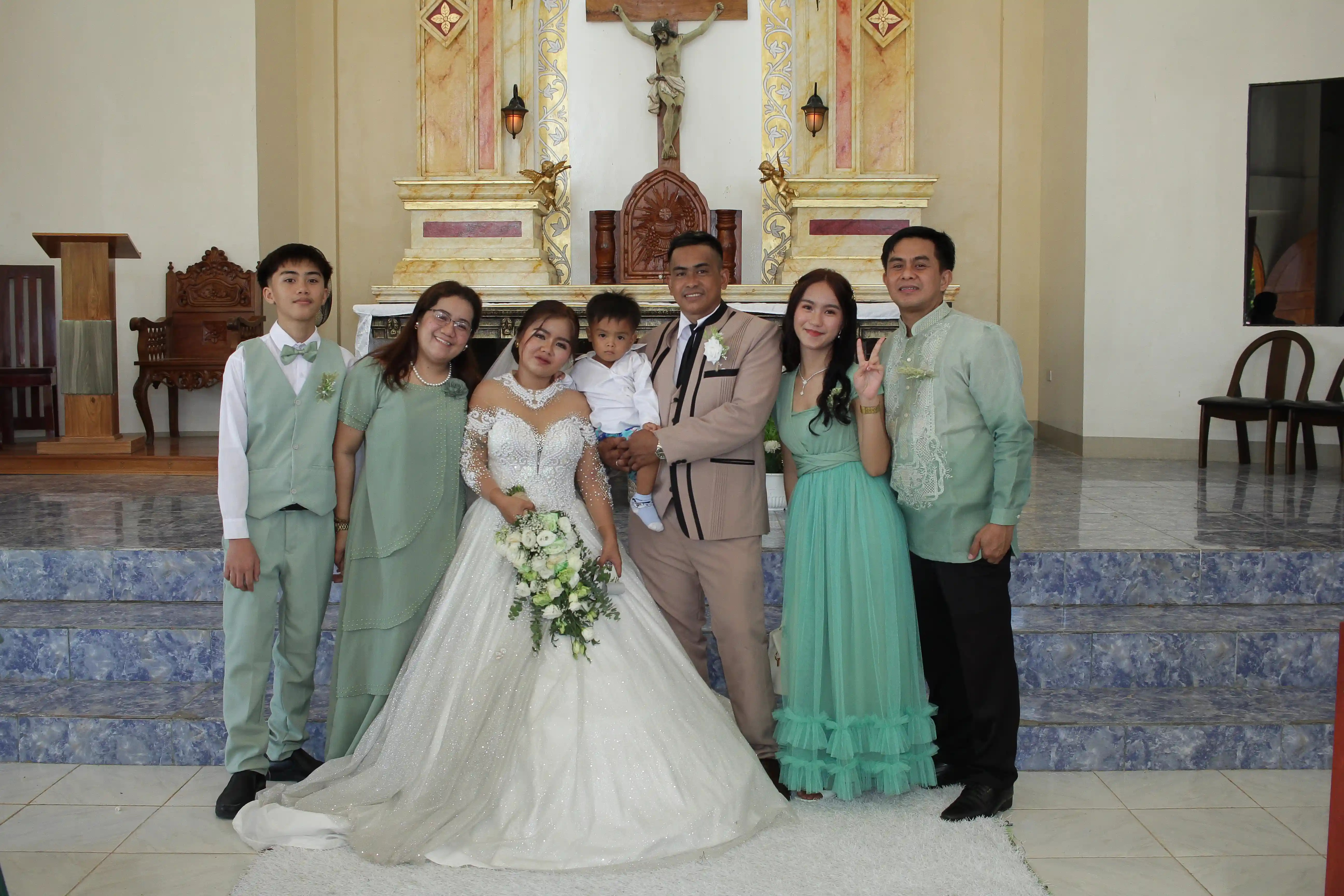 Ninong and Ninang Atanoza family posing with newlyweds John Aries Almendras and Lyka Isabel Bastida in front of the gilded altar of Our Lady of Fatima Mission Area in Socorro Oriental Mindoro