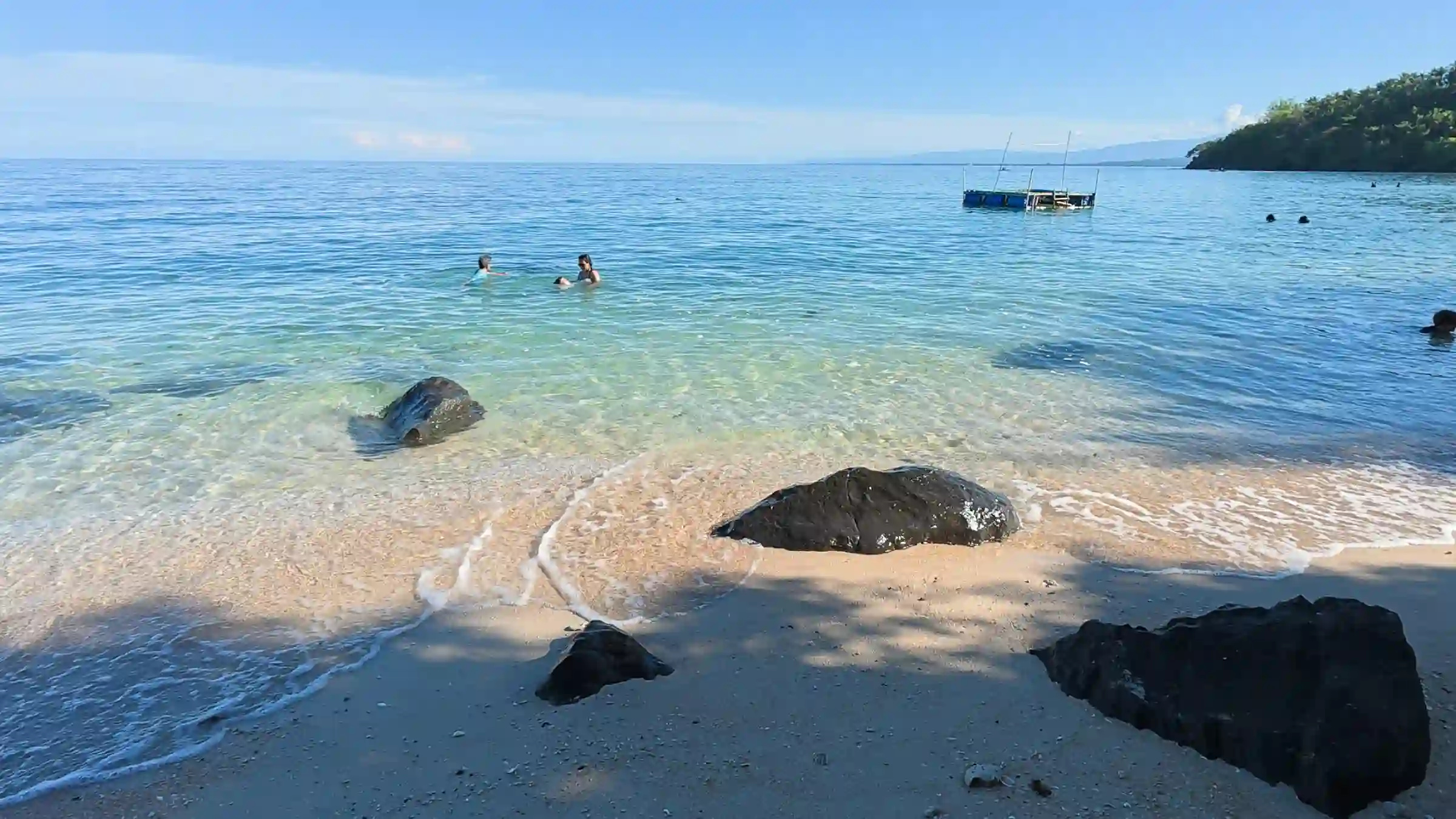 Visitors swimming in clear turquoise water among rock formations at Pili Beach Pinamalayan Oriental Mindoro with a floating raft and forested headland in the background