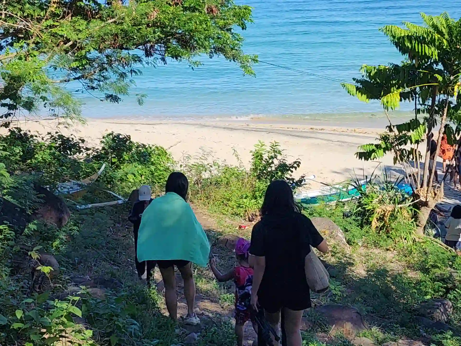 Group of visitors descending a tree lined dirt path toward the cream sand shoreline of Pili Beach in Pinamalayan Oriental Mindoro