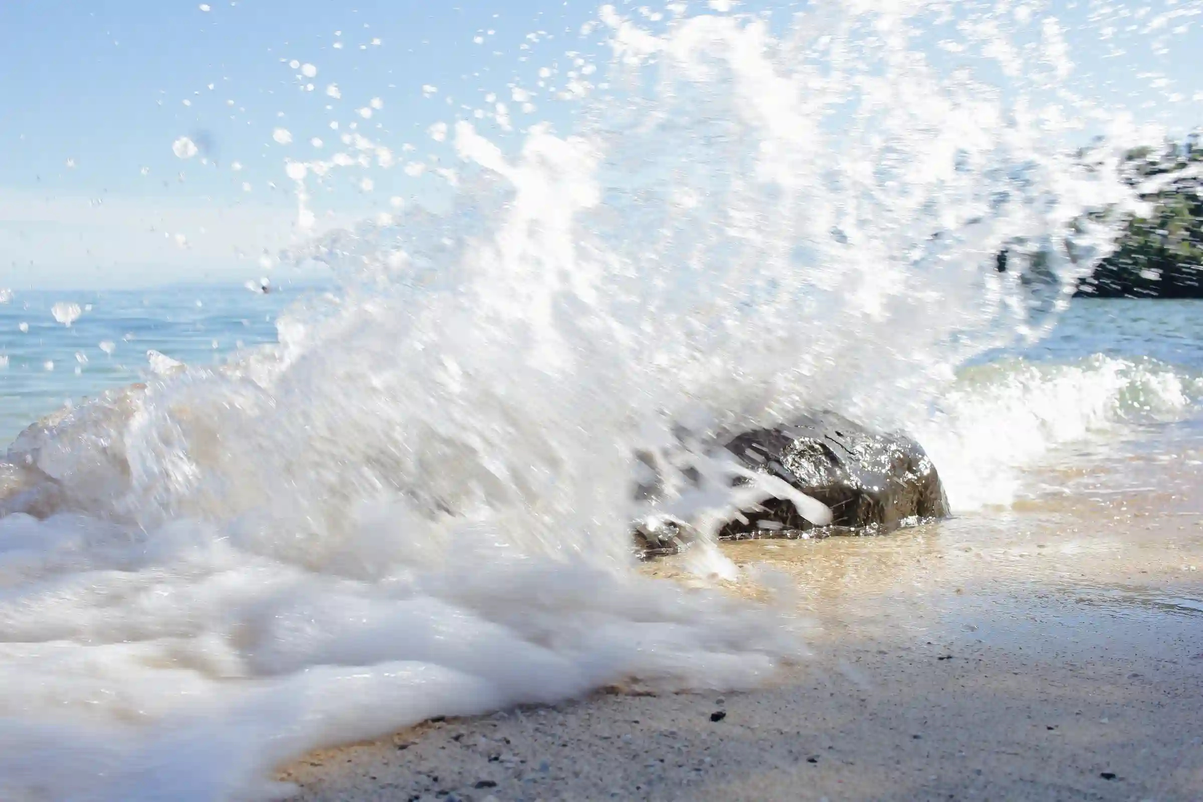 Wave crashing and spraying white foam over a dark rock on the cream sand of Pili Beach in Pinamalayan Oriental Mindoro