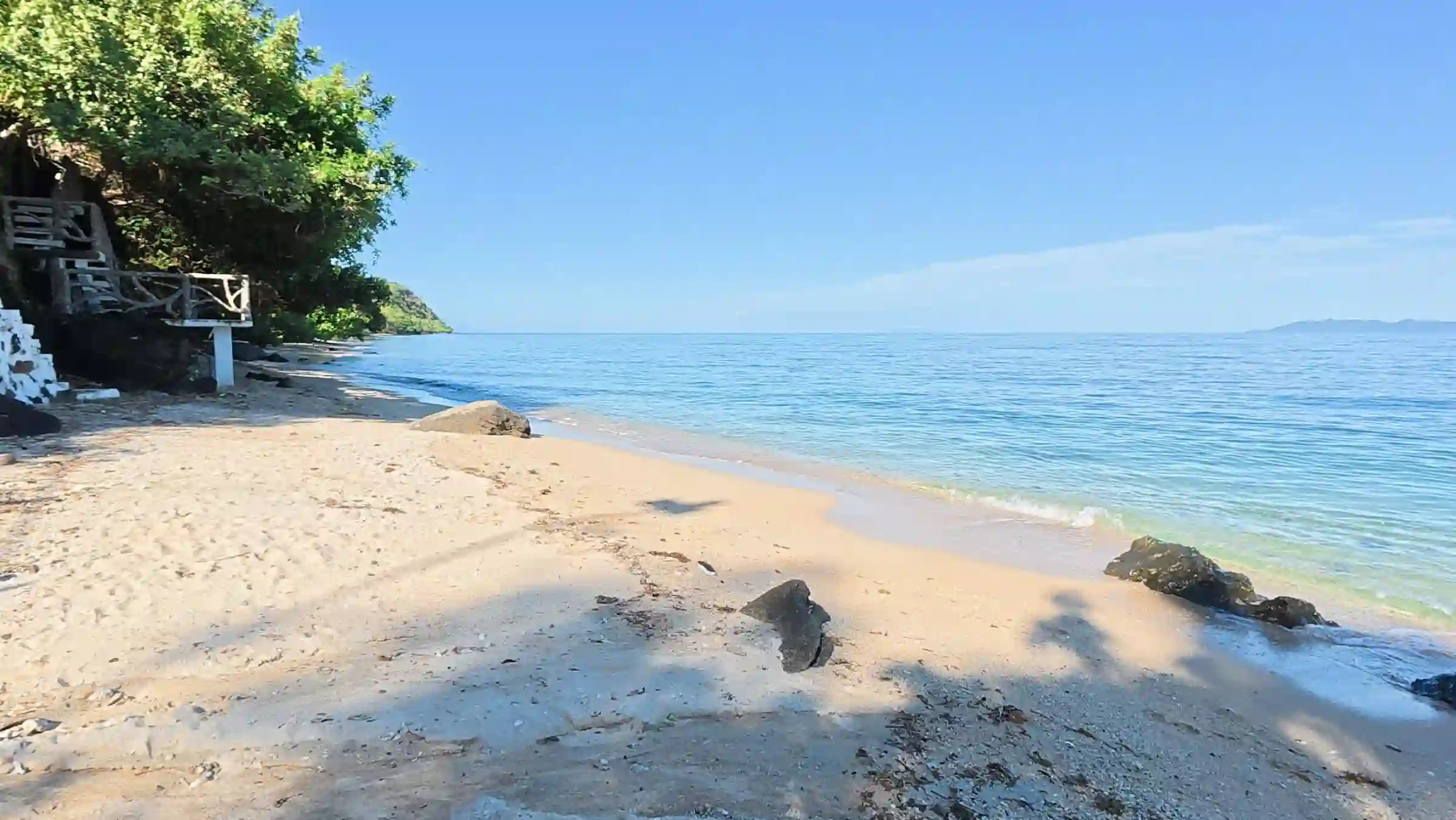 Cream sand and rock formations with clear turquoise water and Conception Island on the horizon at Pili Beach Pinamalayan Oriental Mindoro