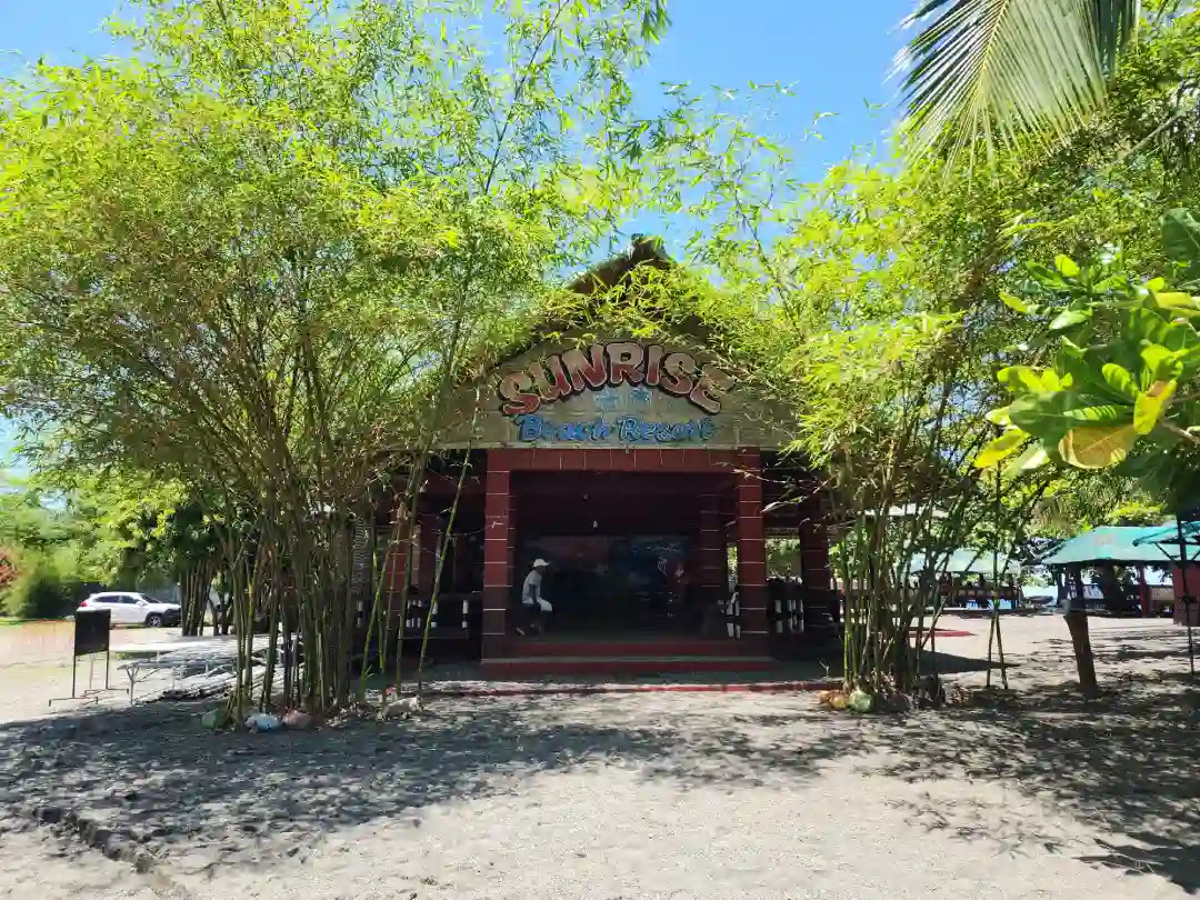 Open function hall building with Sunrise Beach Resort painted signage framed by bamboo trees on dark sand in Pili Pinamalayan Oriental Mindoro