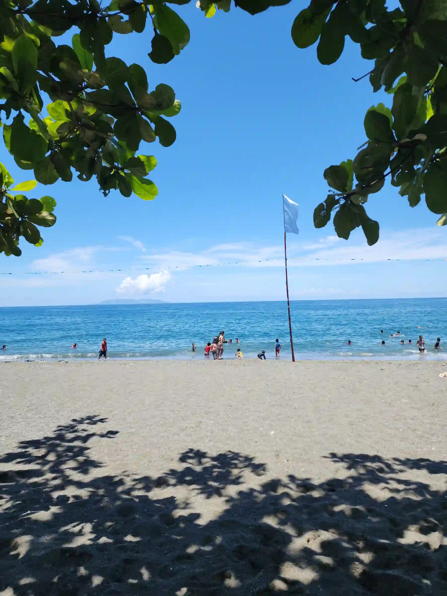Families and children swimming along the wide dark sand shore at Sunrise Beach Resort in Pili Pinamalayan Oriental Mindoro