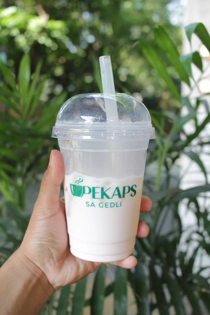 Hand holding an iced Pekaps sa Gedli drink in a clear cup with a dome lid in Manila