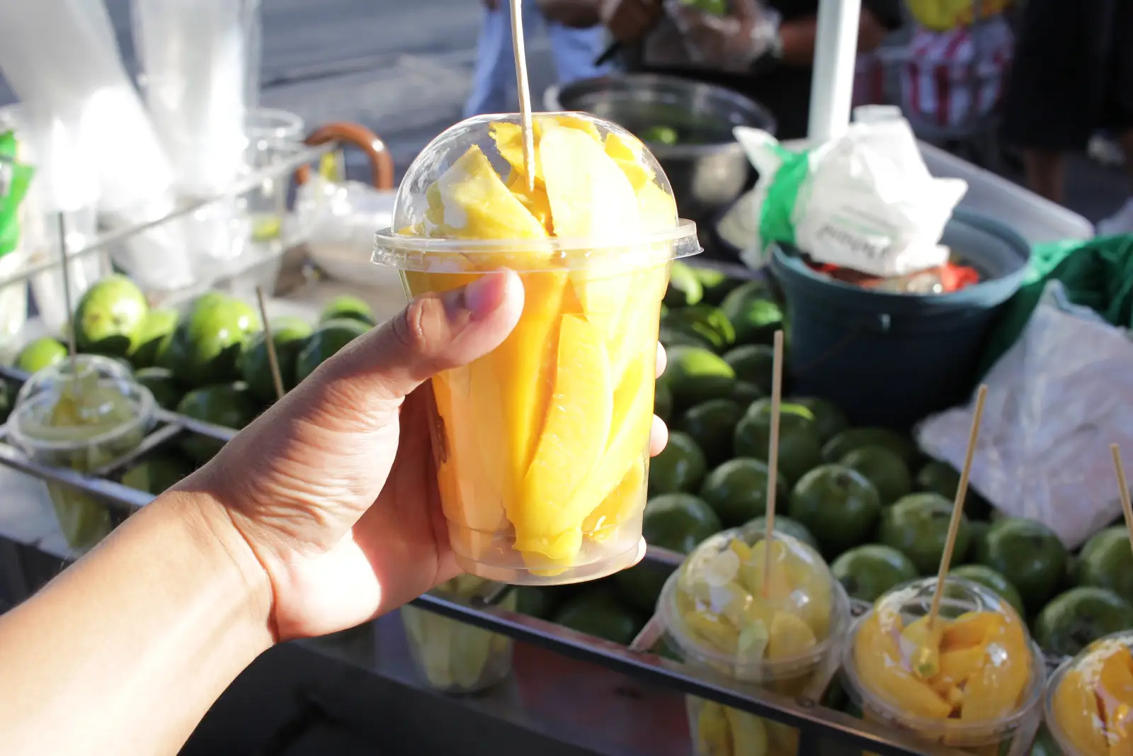Hand holding a cup of sliced ripe mango on a stick at a street fruit stall in Manila
