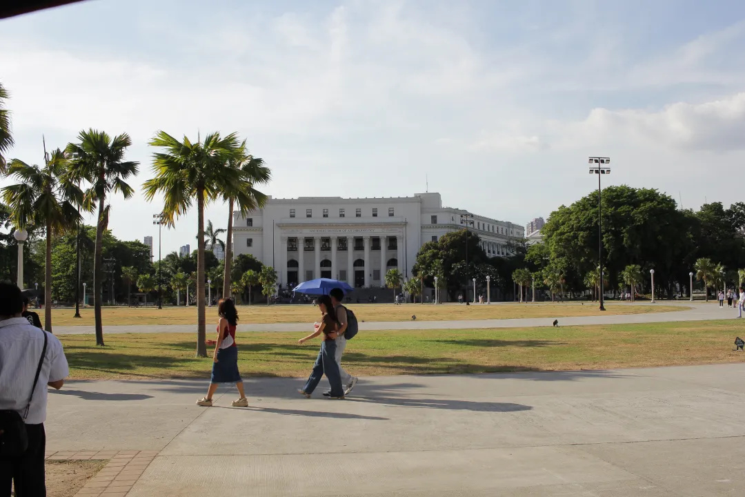 Wide view of National Museum of Anthropology grounds with people walking near palm lined paths in Manila