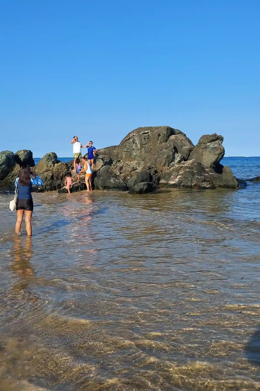 Beachgoers climbing dark volcanic rock formations along the shoreline near Jomalig Island