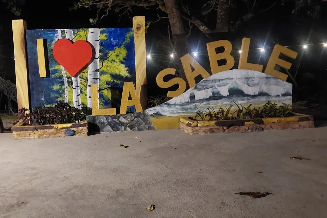Illuminated I Love La Sable resort sign strung with lights among trees at night in Jomalig
