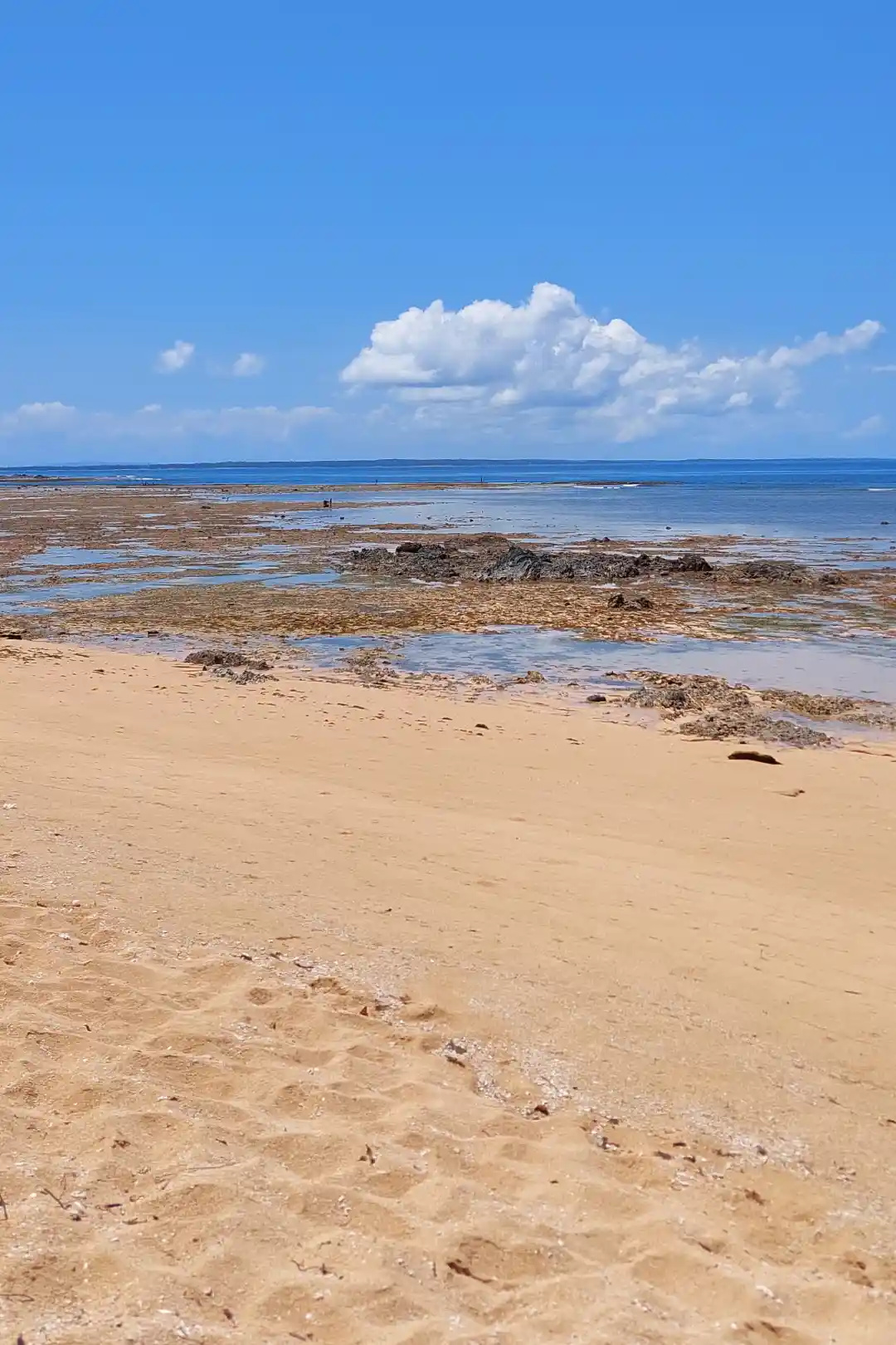 Low tide reef flat and golden sand stretching toward the horizon in Jomalig Island