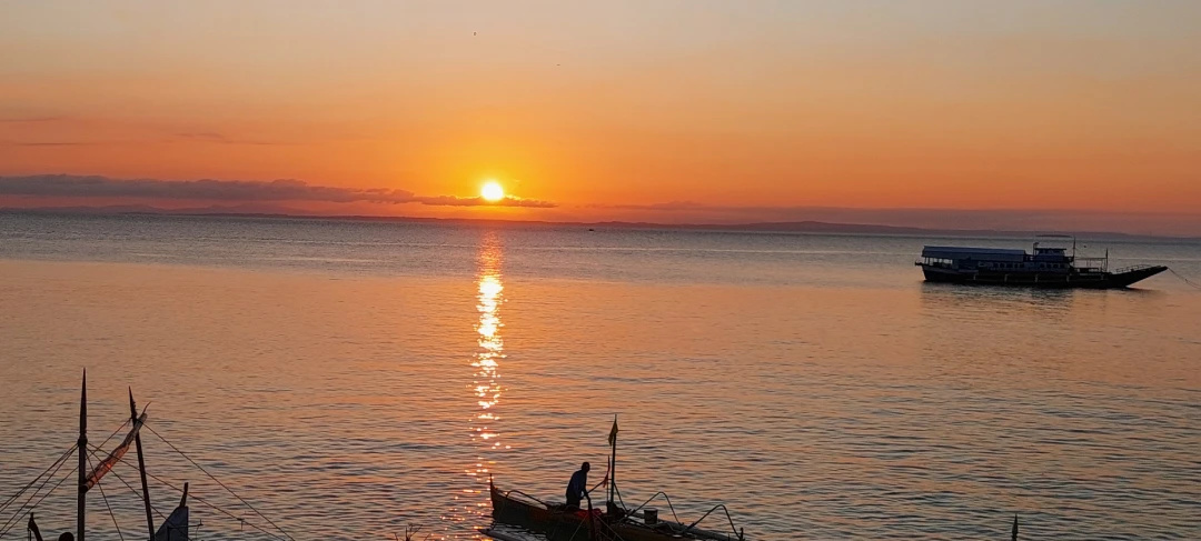 Sunset over calm water with silhouetted fishing boats near the shore of Jomalig Island