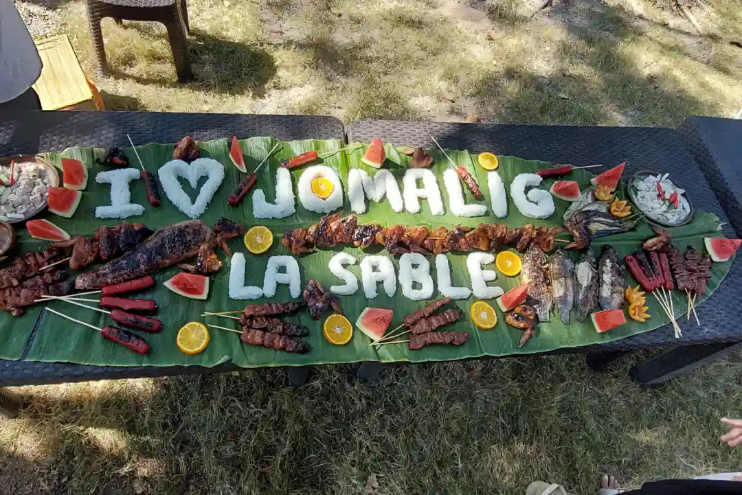Grilled meat fish and fruit arranged on banana leaves spelling I Love Jomalig La Sable