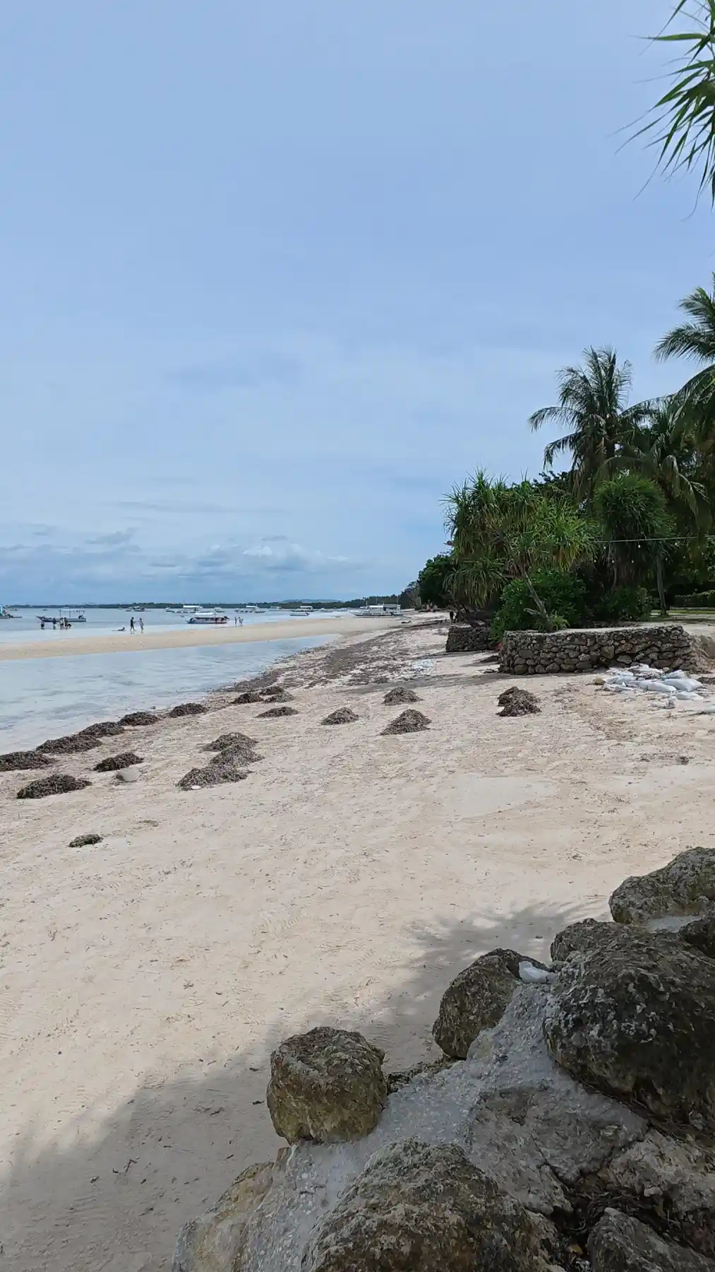 Low tide shoreline with anchored boats and beachgoers wading at Doljo Beach in Panglao, Bohol