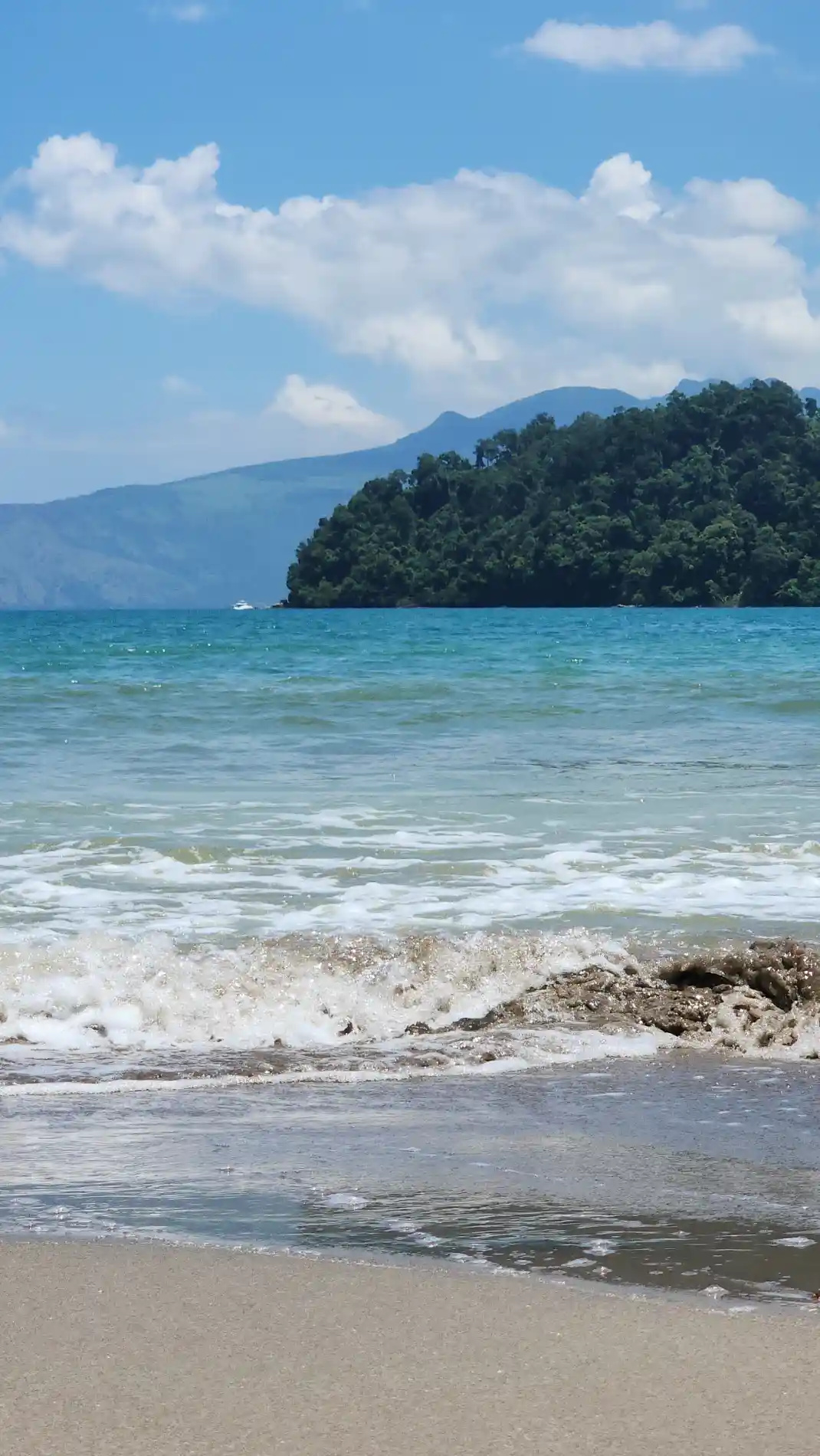 Waves curling onto open sandy shore beneath tree covered hills along the coast of Morong, Bataan