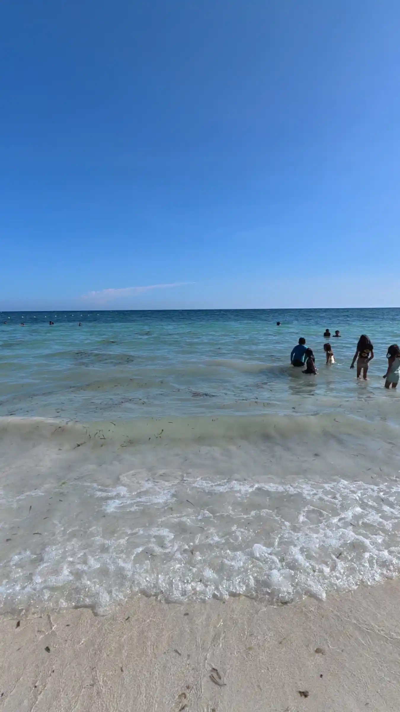 Family wading in turquoise water with a foam edged wave reaching the sand at Kalipayan Beach Panglao