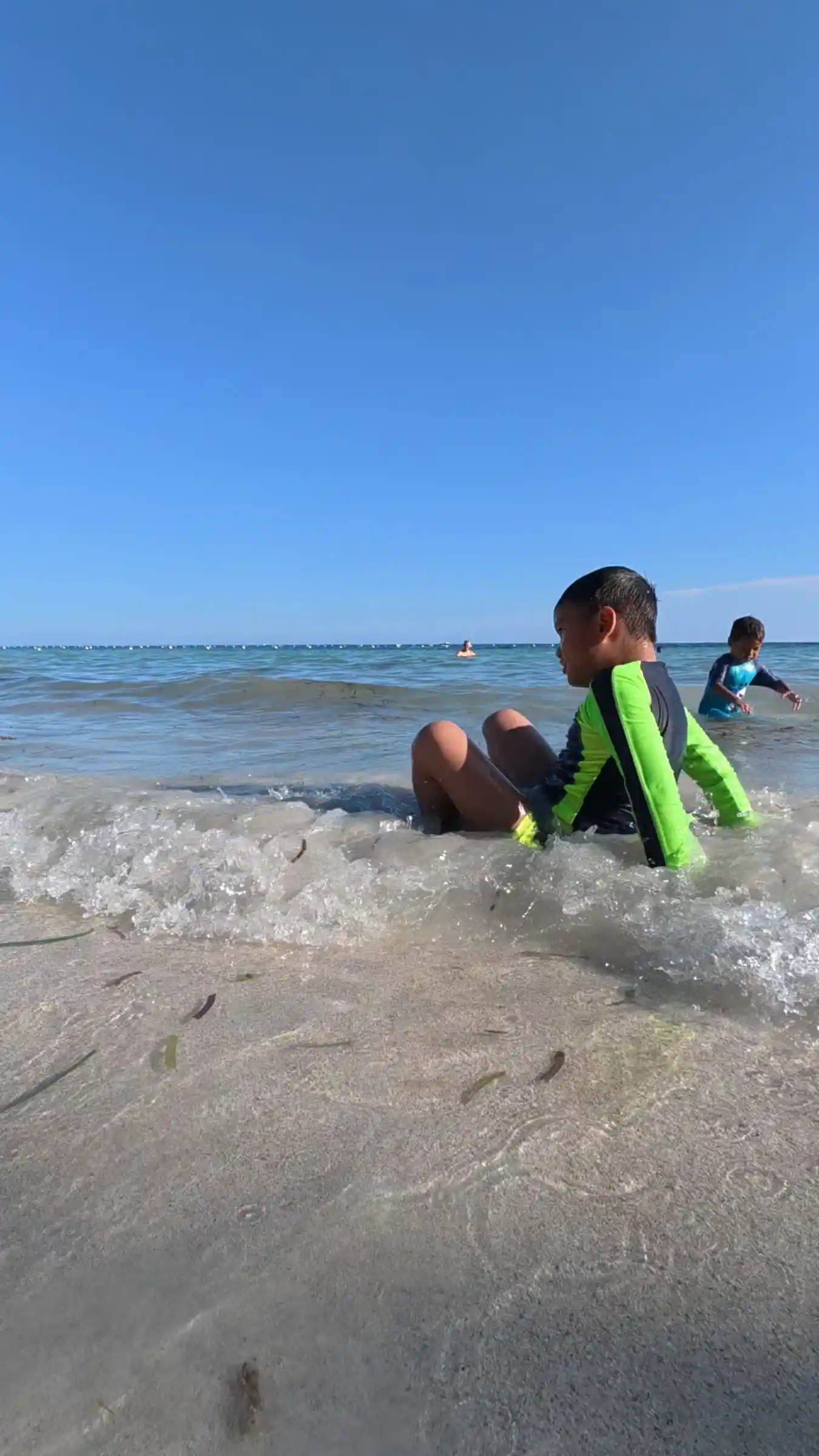 Two boys sitting in a breaking wave at the shoreline of Kalipayan Beach Panglao Bohol
