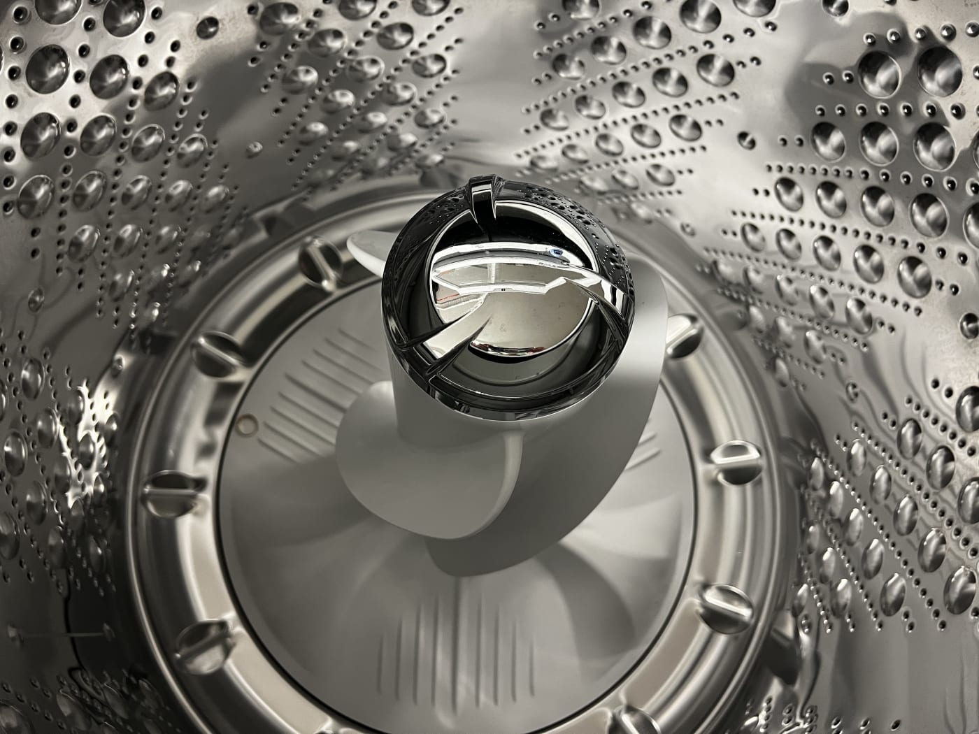 Looking down into the empty stainless steel drum of a top-loading washing machine.