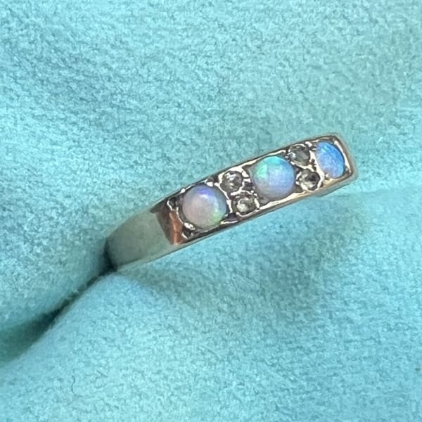 A slim gold band set with three opals and four tiny diamond chips, resting on pale blue fabric.
