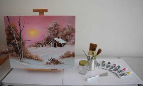 Painting on easel with Bob Ross paints and brushes displayed