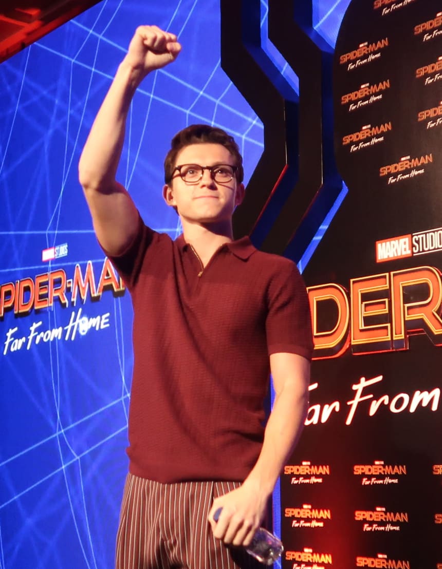 Tom Holland raising his fist on stage at a Spider-Man: Far From Home event in Bali, 2019