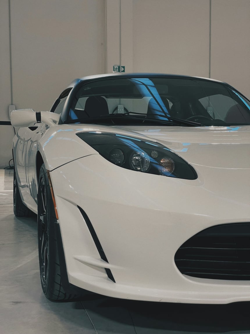 White original Tesla Roadster parked indoors at a Tesla center in Verona, Italy