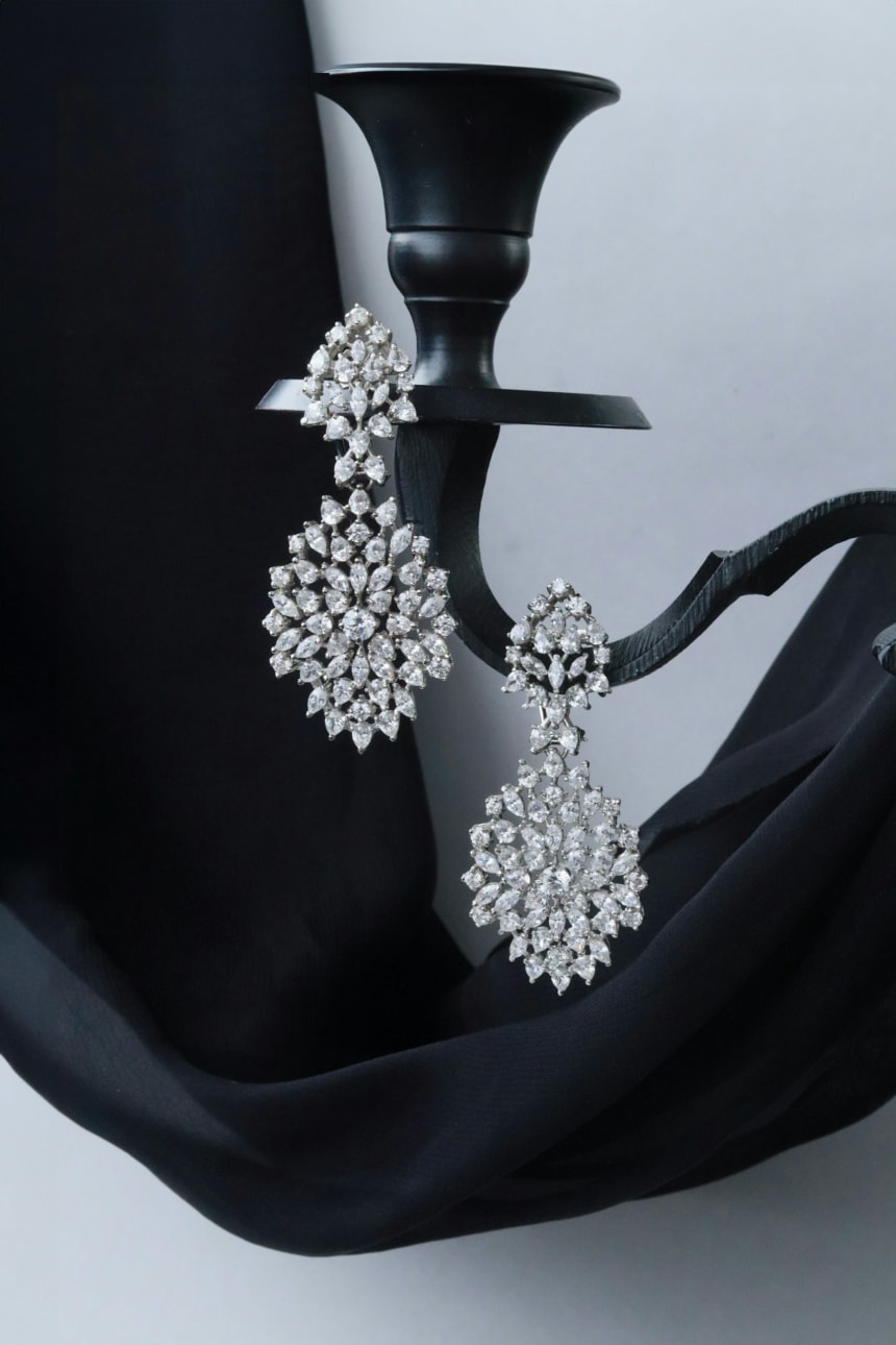 Pair of sparkling diamond drop earrings hanging from a black jewelry stand