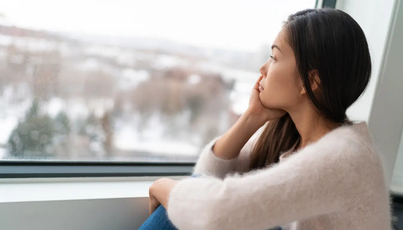 Young expat woman gazing out the window, feeling homesick.