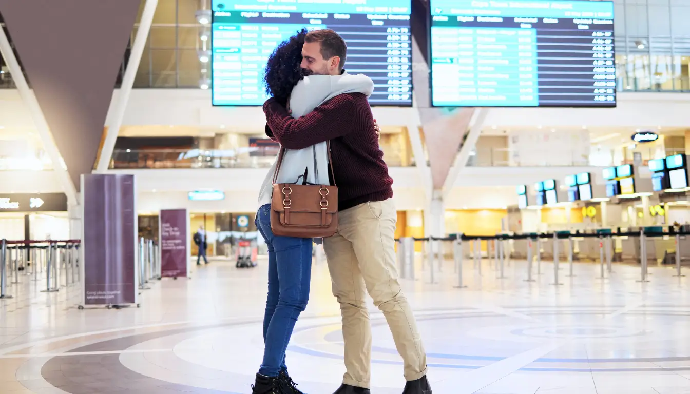 A long-distance couple hugging at the airport, symbolizing the excitement of planning in-person visits to strengthen their relationship.