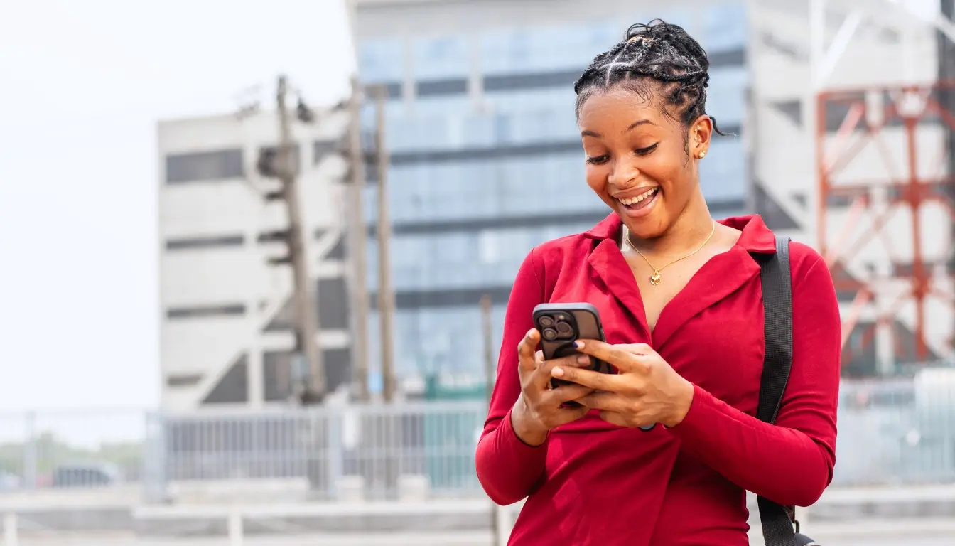 A woman outdoors, surprised and delighted while reading a message, symbolizing the joy of surprises in a long-distance relationship.