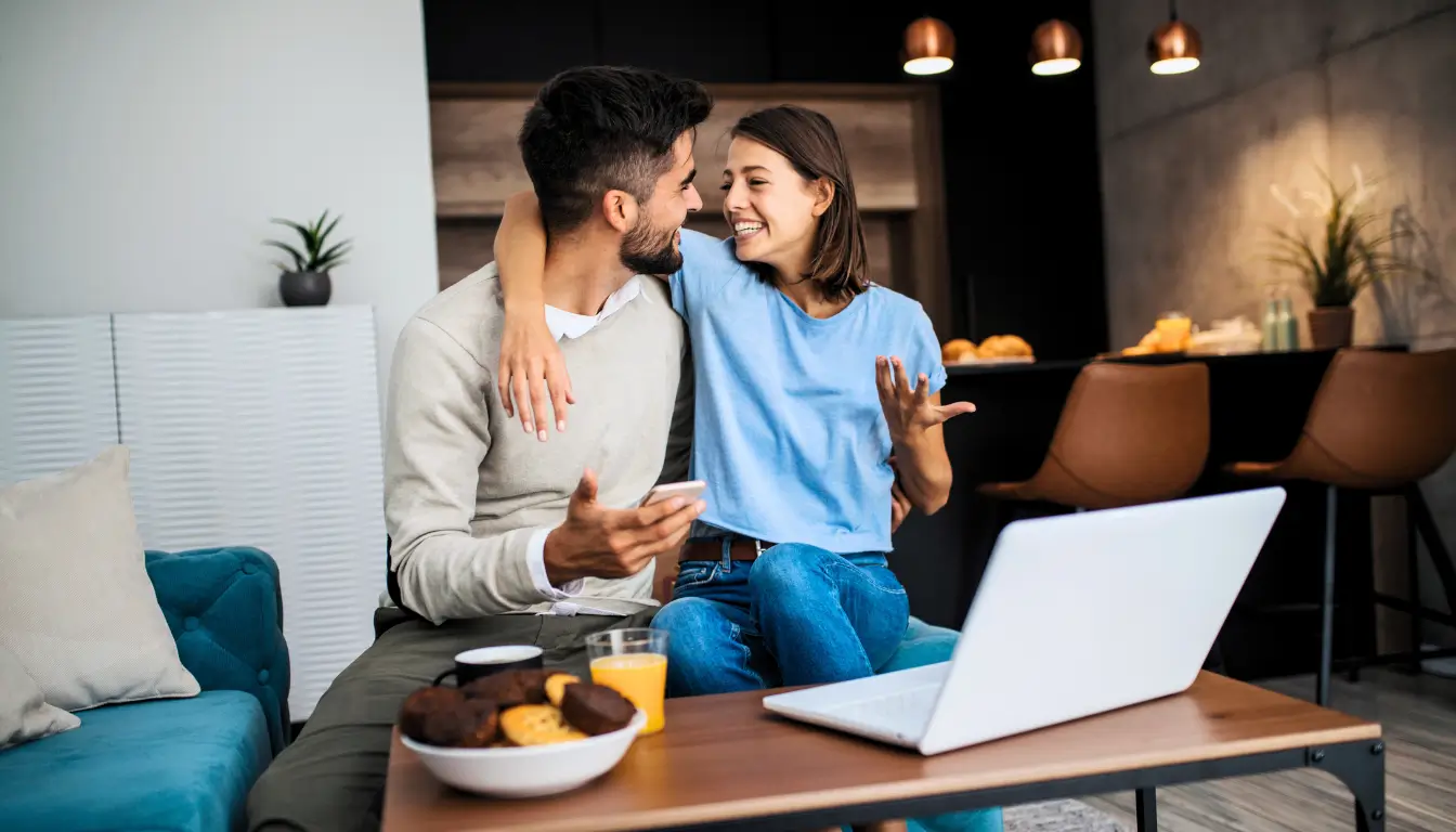A happy couple hugging and laughing on a couch, symbolizing a former long-distance couple who successfully moved in together.