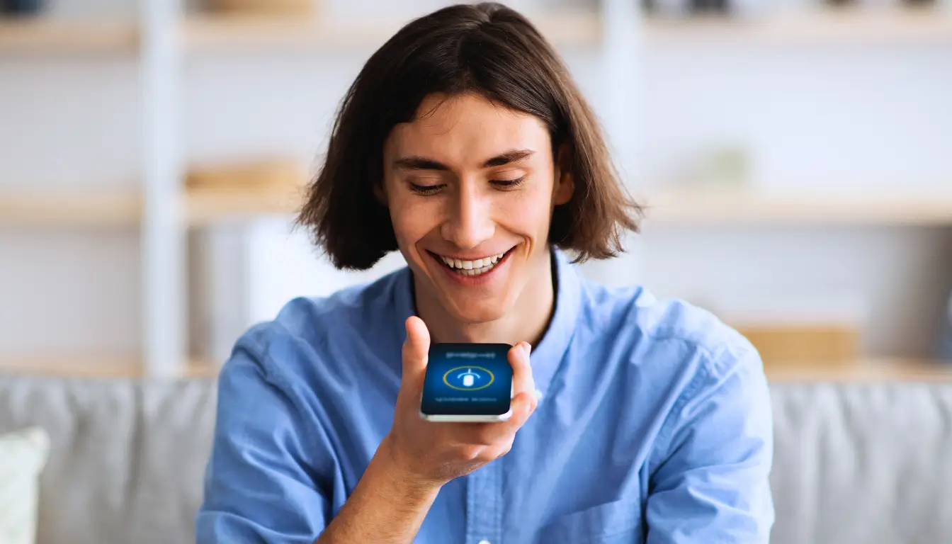 Smiling man recording a voice message on his phone, sharing an audio diary with his long-distance partner.