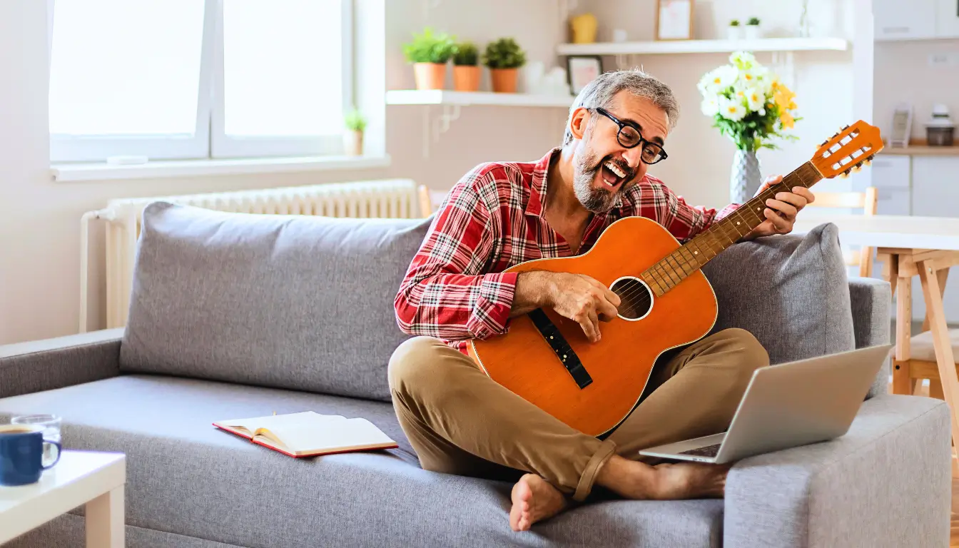 Smiling man playing guitar on a video call, sharing his hobby with a long-distance partner.