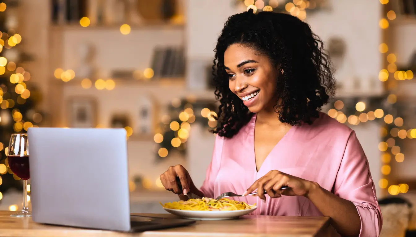 Woman smiling during a virtual dinner date with her long-distance partner, with food and wine.