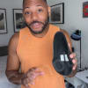 Person in orange shirt holding a black shoe indoors.