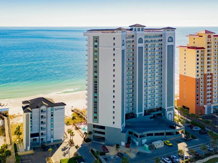 Aerial view of Gulf-front condo towers and a beachfront pool in Gulf Shores, Alabama, beside emerald Gulf water