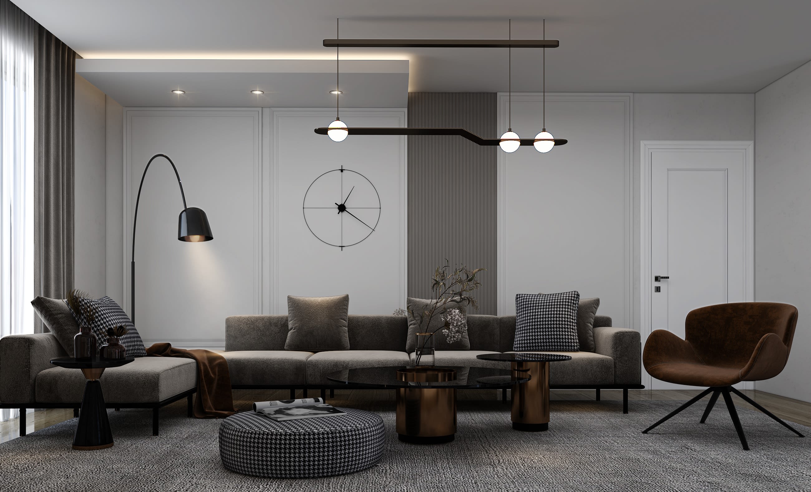 The image shows a modern and minimalist living room interior. The room features a gray L-shaped sofa with various decorative pillows, a round black and white patterned ottoman, and a low wooden coffee table. The walls are painted in a light gray color, and there is a large wall clock with a simple black outline design. The lighting in the room is provided by a suspended linear light fixture with multiple bulbs. Overall, the space has a sophisticated and monochromatic color scheme with a focus on clean lines and minimalist design elements.