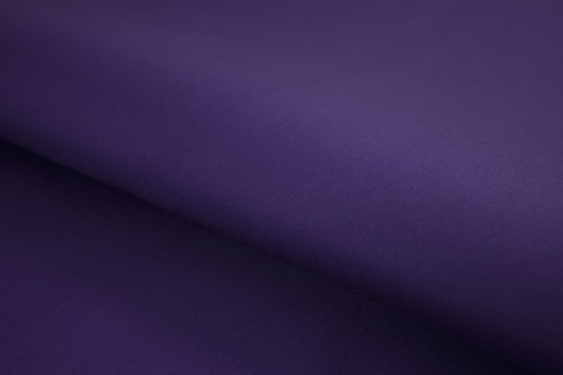 Close-up of royal purple wrinkle-resistant cotton shirt fabric with smooth fine weave texture