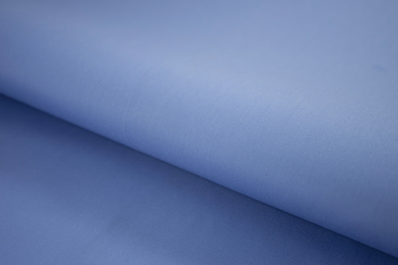 Close-up of classic blue wrinkle-resistant cotton shirt fabric with smooth fine weave texture