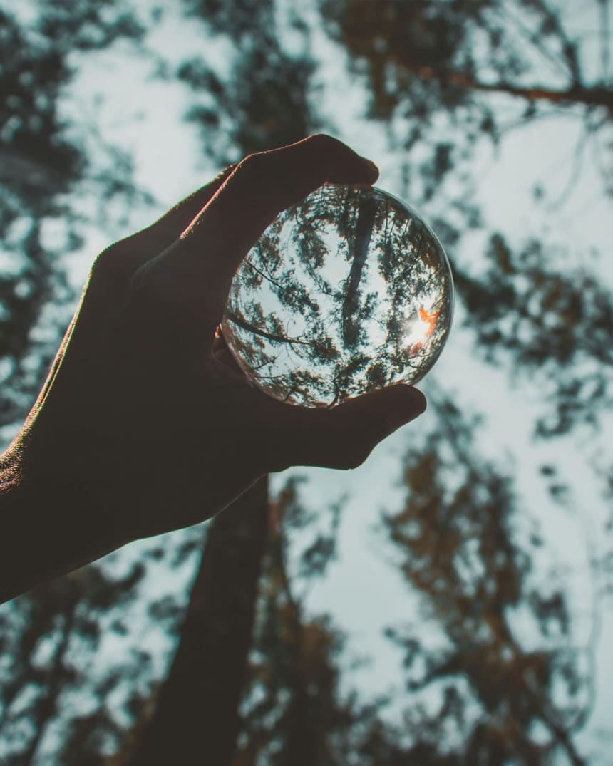 Boule de verre tenue dans une forêt, lumière naturelle