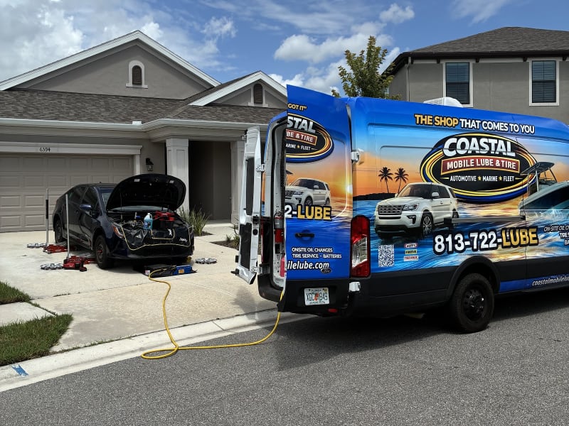 Driveway oil change from the Coastal van, hood up on a customer's sedan