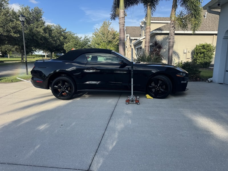 Black Mustang convertible jacked for tire service in a customer's driveway