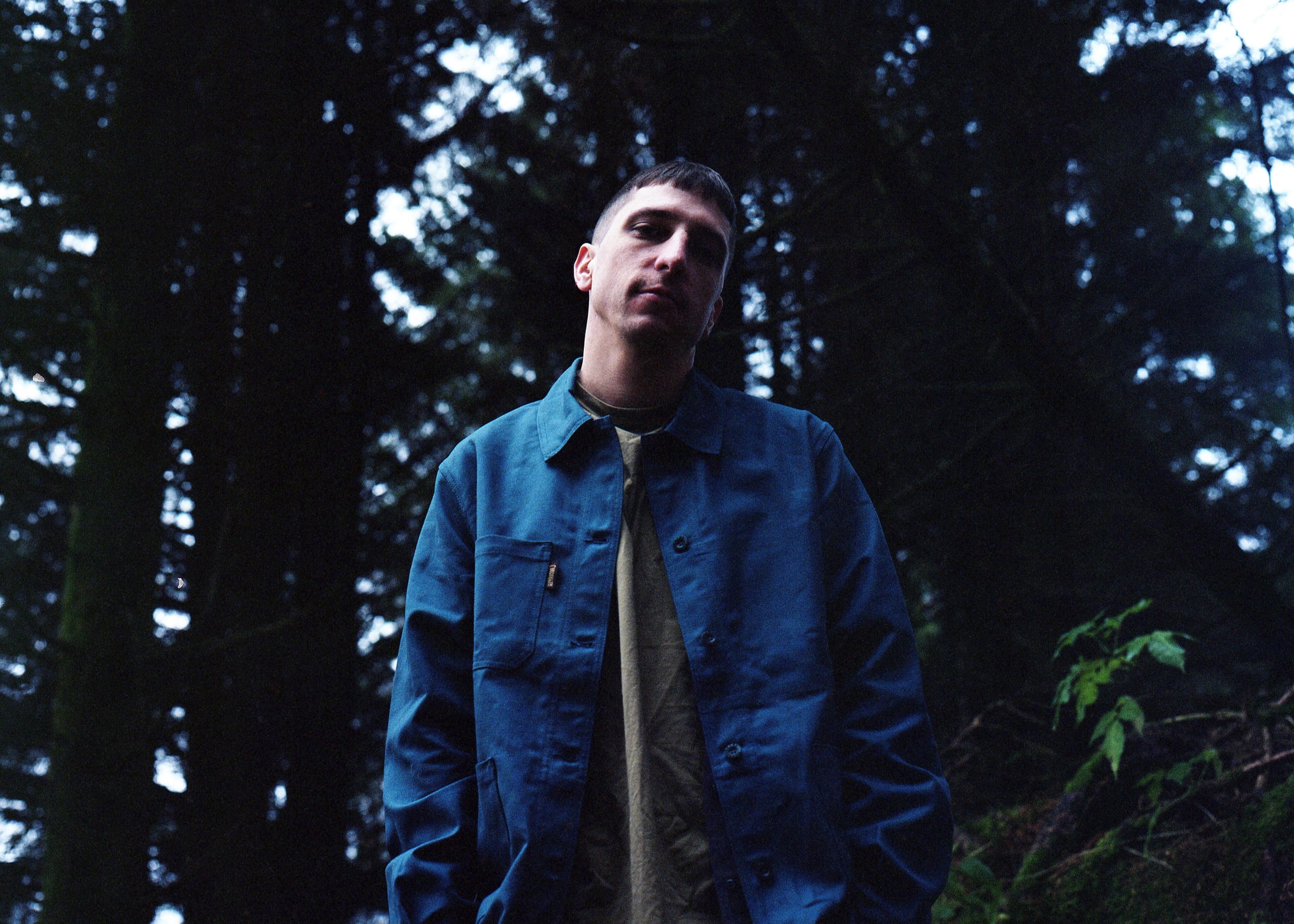 A portrait image of Lewis Lowe, pictured in a green forest environment.