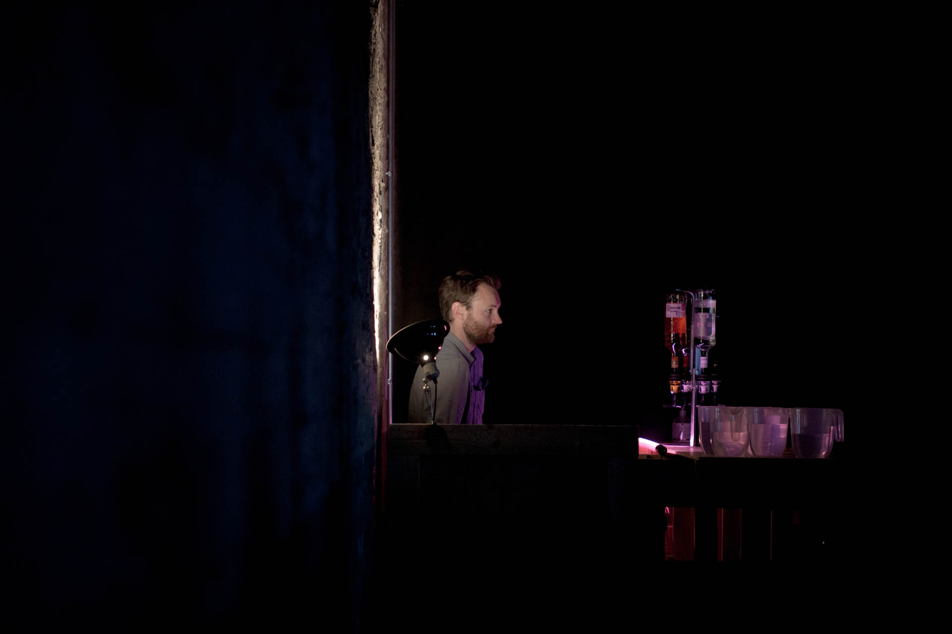 Man reclines against wall behind bar in darkness